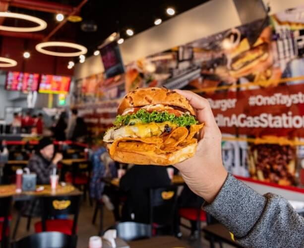 Someone holding a Taystee's Burger 